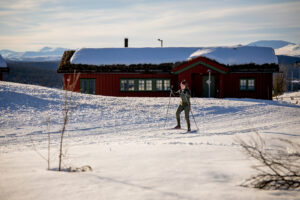 Langrennsløper på Gålå foran rød fjellstue i vinterlandskap
